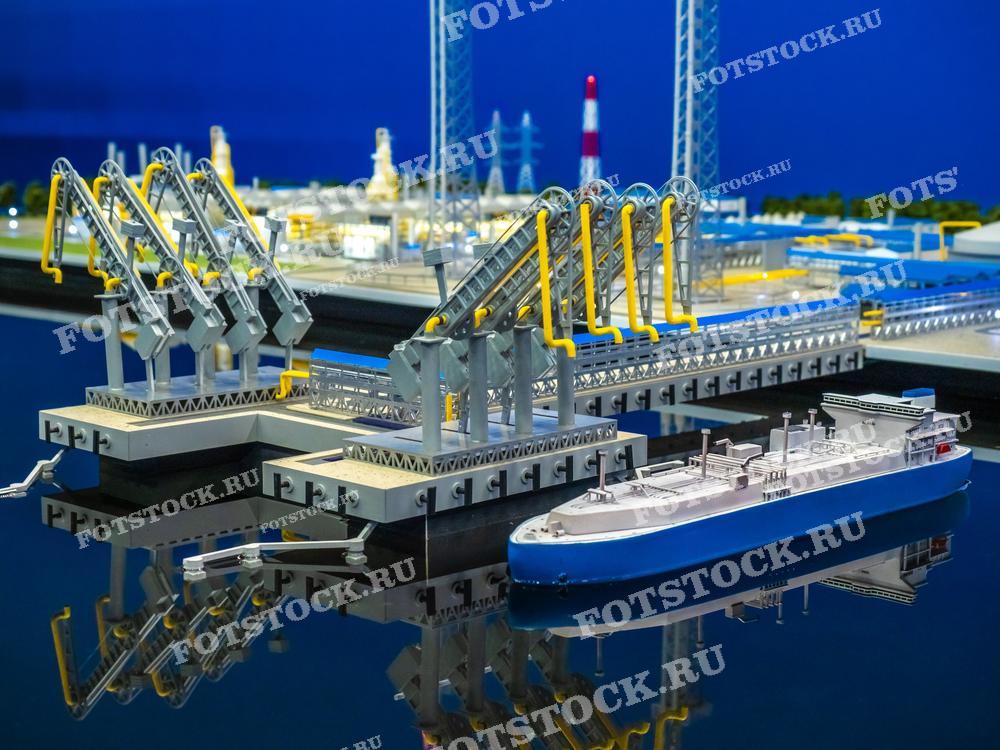 На изображении представлен макет морского порта с грузовым судном, пришвартованным у причала. В макете видны погрузочные краны и элементы инфраструктуры порта. Фотография иллюстрирует архитектуру и логистику портовой деятельности.